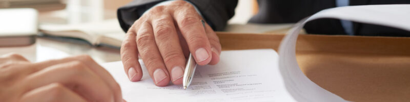 Close-up of businessman examining business contract and signing it at the office desk